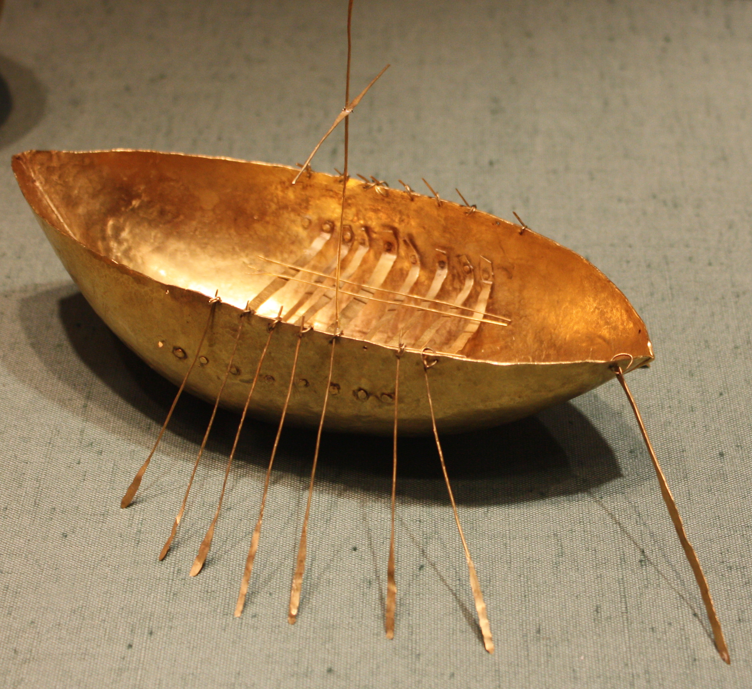 [Image: Solid gold model of a rowed and single-masted ship or boat, with a rudder, and nine pairs of oars.]